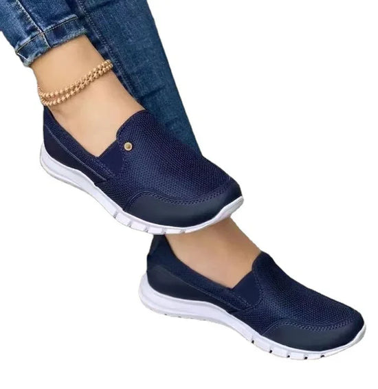 Navy blue mesh slip-on sneakers with white soles and slim fit, paired with denim jeans.