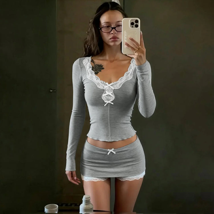 Woman wearing a fitted grey long sleeve top and mini skirt with white lace trim.