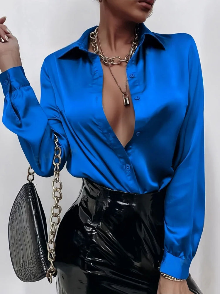 Bold blue satin blouse with deep V-neck, paired with black patent leather skirt, chain necklace