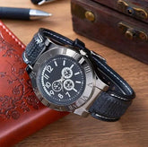 Black leather strap watch with silver case, Roman numerals, and chronograph dial on desk