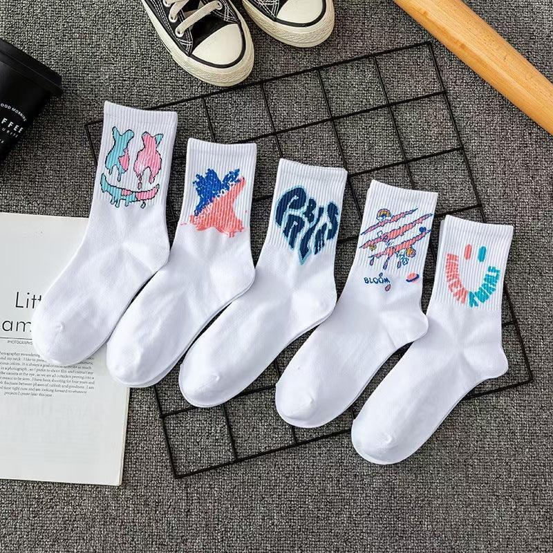 Five pairs of white cotton crew socks with colorful graphic prints, laid out on a gray fabric surface.