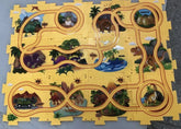 Colorful puzzle mat with a dinosaur-themed track, featuring cartoon dinosaurs, eggs, volcanoes, palm trees, and a safari jeep on a yellow background.