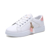 White low-top sneaker with pink heel accent, lace-up design, and tassel charm detail.