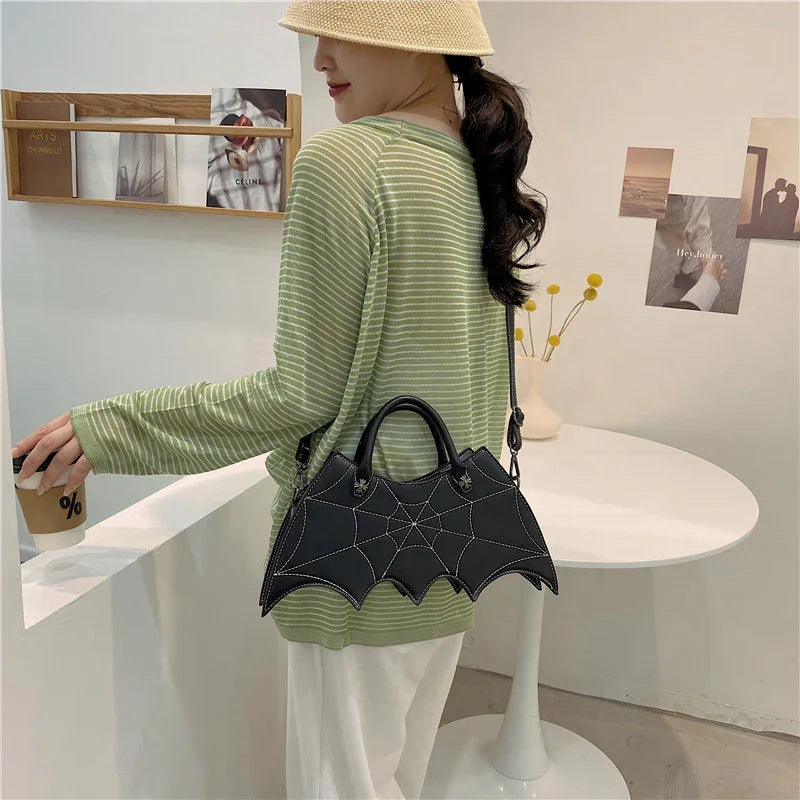 Woman in loose green striped long sleeve top and white pants, wearing a unique black bat wing-shaped handbag, casual streetwear style