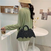 Woman in loose green striped long sleeve top and white pants, wearing a unique black bat wing-shaped handbag, casual streetwear style