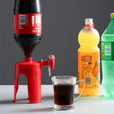 Red plastic soda dispenser for bottles with tap, dispensing cola into a glass, with other soft drinks nearby.