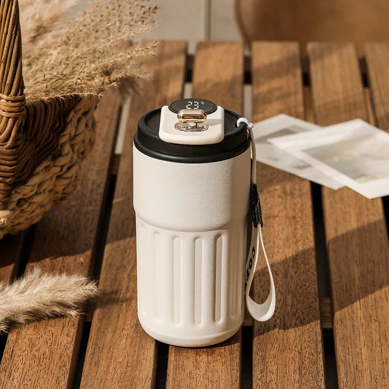White insulated travel tumbler with digital temperature display and wrist strap on wooden table