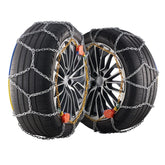 Pair of car tires with metal snow chains on black alloy rims, isolated on white background.