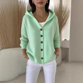 Woman wearing a mint green knit hooded cardigan with brown buttons and white pants