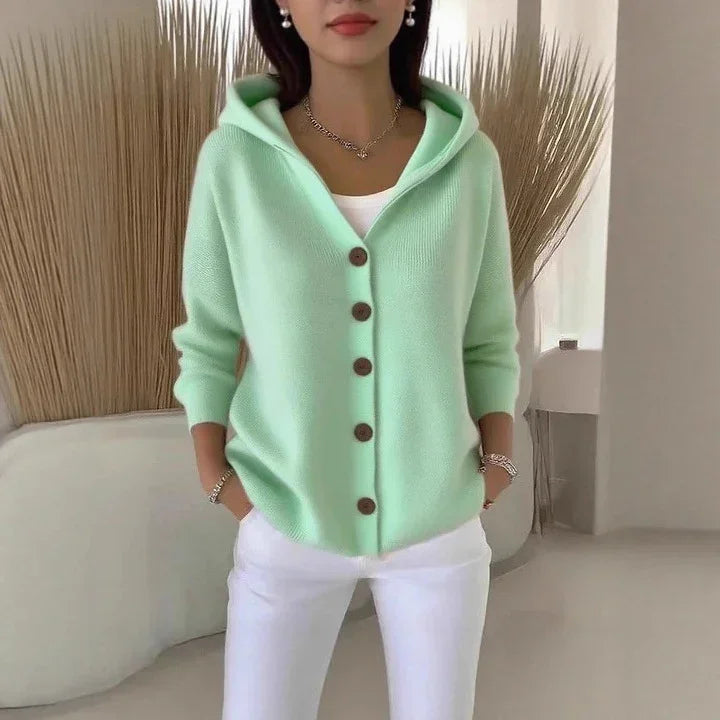 Woman wearing a mint green knit hooded cardigan with brown buttons and white pants