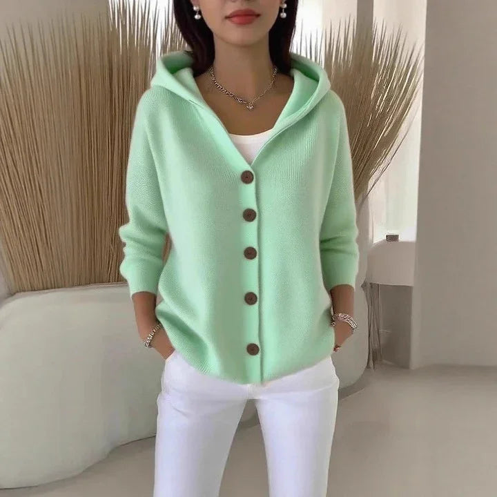 Woman wearing a mint green knit hooded cardigan with brown buttons and white pants