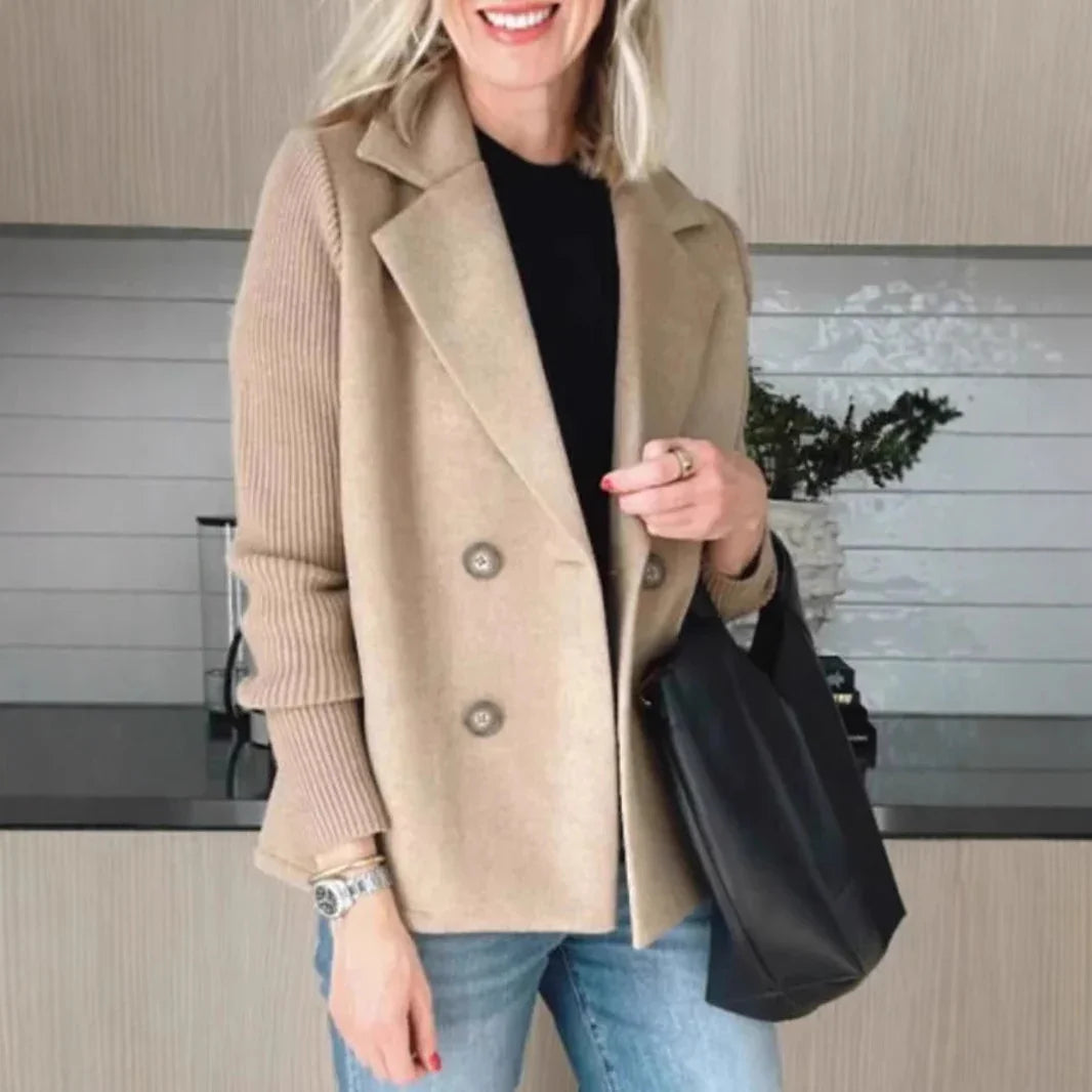 Woman wearing a beige double-breasted wool blend blazer with ribbed sleeves, black top, and light blue jeans.