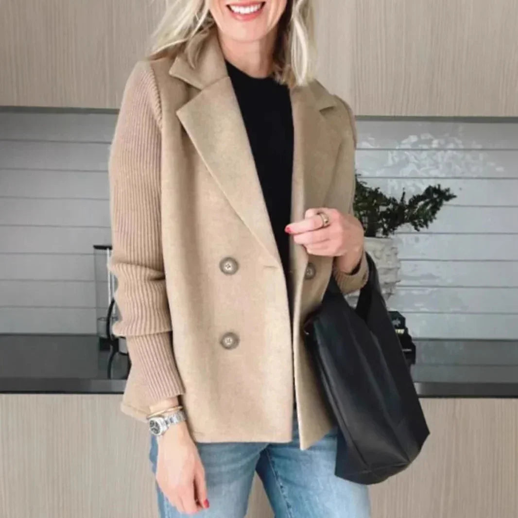 Woman wearing a beige double-breasted wool blend blazer with ribbed sleeves, black top, and light blue jeans.