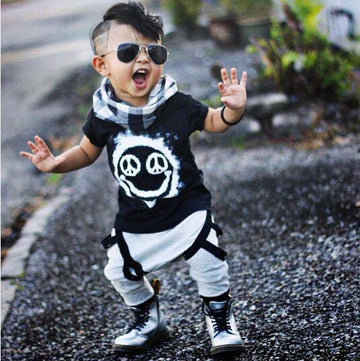 Toddler in black graphic tee, gray jogger pants with straps, scarf, and boots, streetwear style