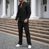 Man wearing a black textured button-down shirt and matching pants set with relaxed fit and white sneakers.