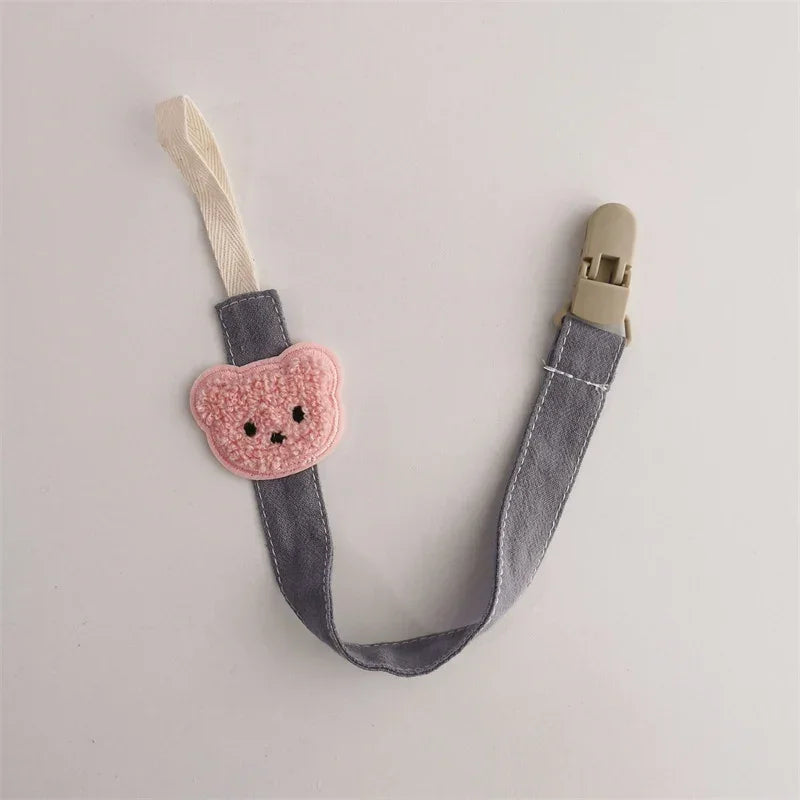 Gray fabric pacifier clip with pink bear patch and beige plastic clasp, cute accessory