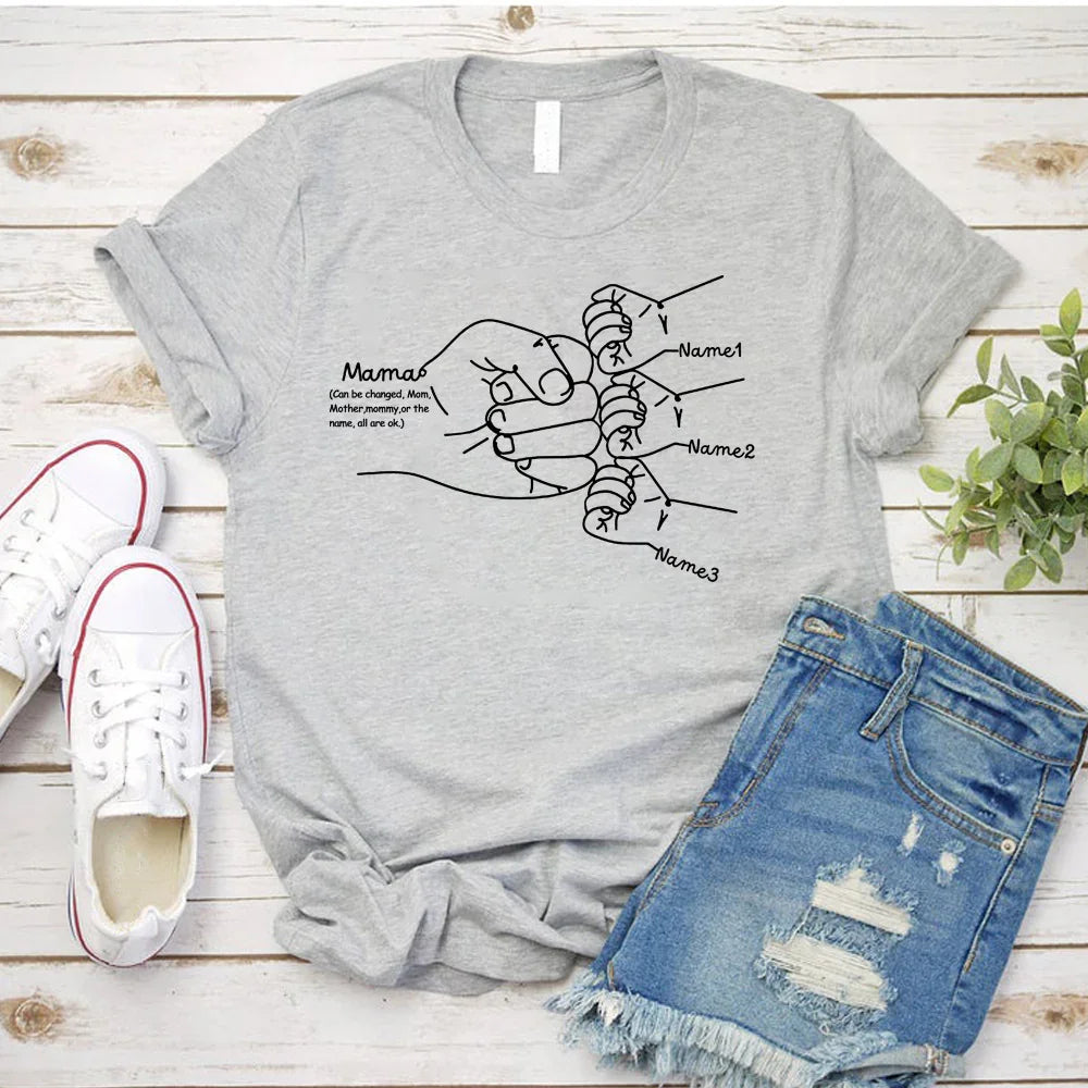 Light gray short sleeve graphic tee with mother and child hand illustration, paired with distressed denim shorts. Casual, relaxed fit streetwear style.