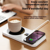 White ceramic mug with coffee on a desk mug warmer and smartphone wireless charging pad.
