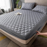 Gray quilted fitted mattress cover with matching pillows on a modern bed