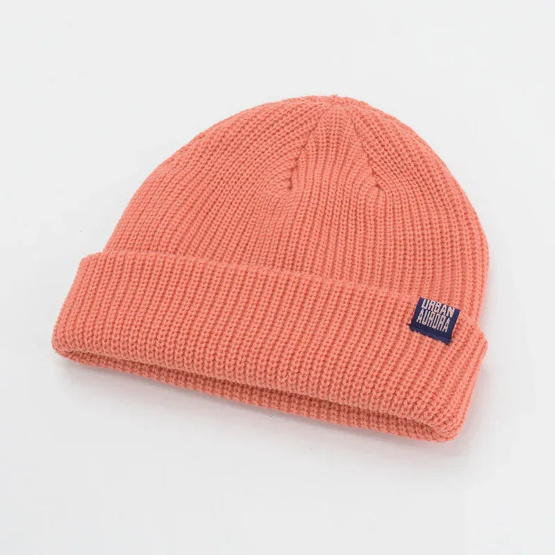 Coral pink knit beanie with ribbed texture and folded cuff, soft streetwear hat.