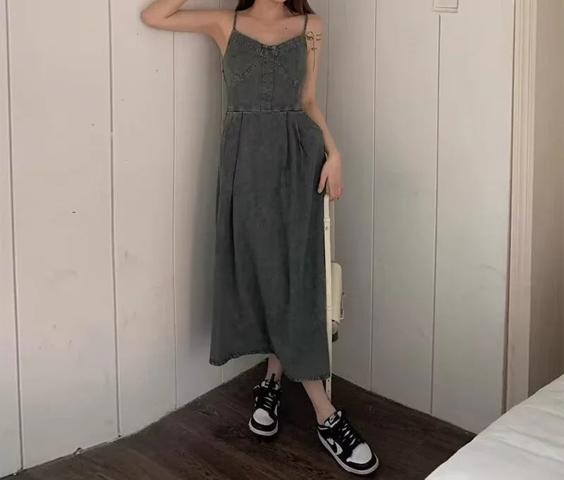 Woman wearing a grey denim midi dress with spaghetti straps and a relaxed fit, paired with sneakers.