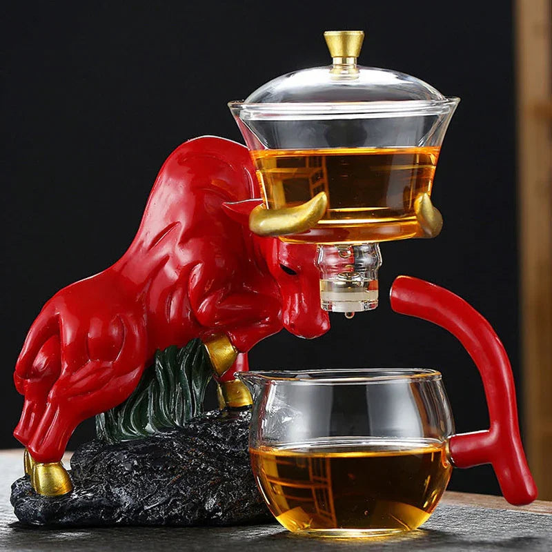 Red bull-shaped tea set with glass teapot and matching glass cup on black surface