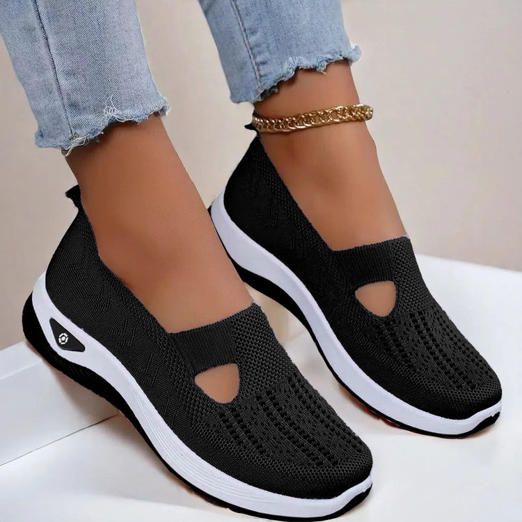 Black mesh slip-on sneakers with white sole, breathable knit material, casual fit, worn with jeans.