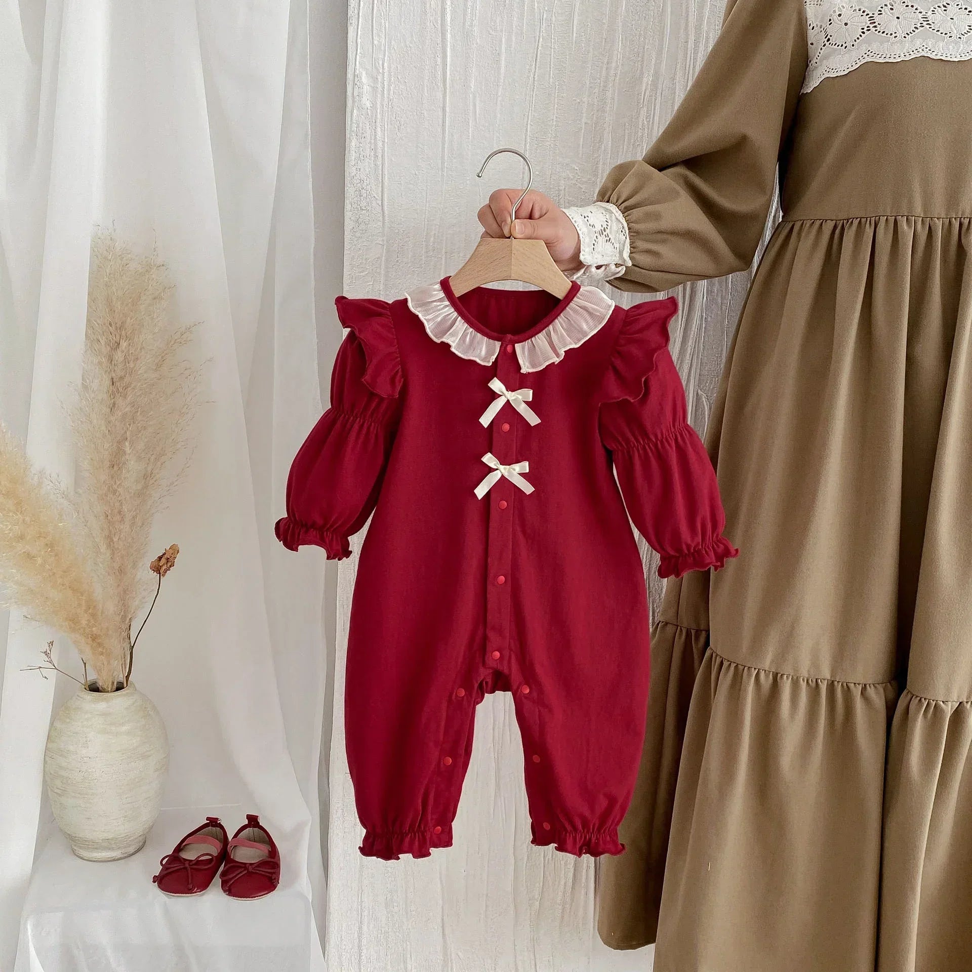 Red baby romper with ruffled long sleeves, white collar and ribbon bows, cotton fabric.