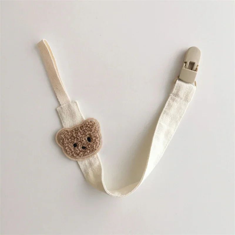 Cream fabric pacifier clip with cute bear patch, beige plastic clasp, minimalist style