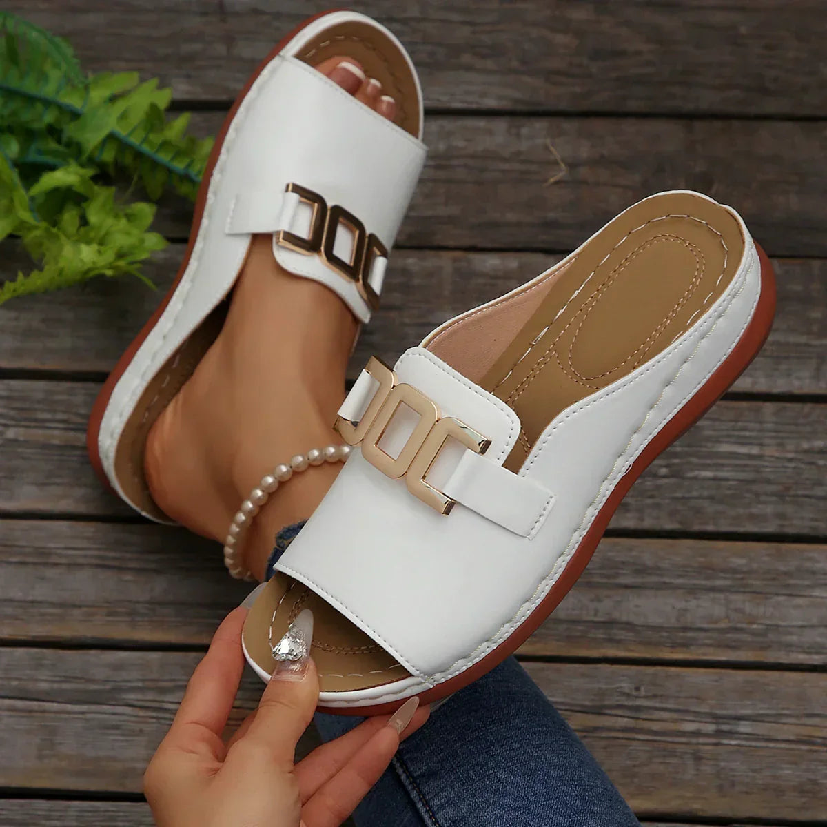 White slip-on sandals with gold buckle detail, cushioned sole, and open toe design