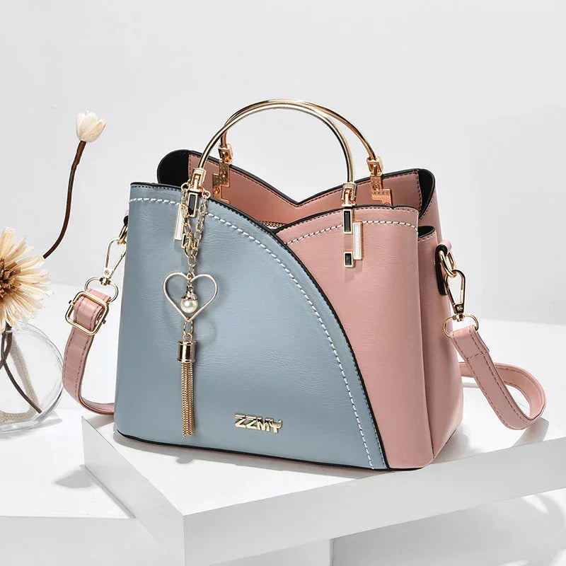 Pastel pink and blue faux leather handbag with gold hardware, top handles, and heart keychain charm.