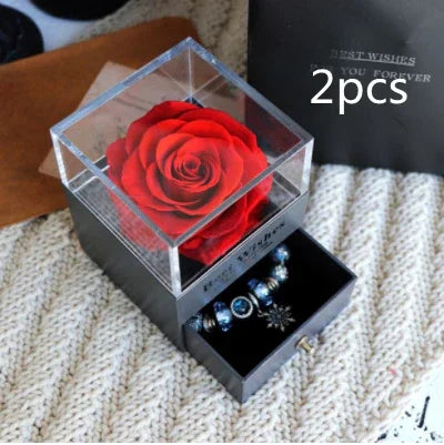 Gift box with a preserved red rose and silver blue charm bracelet inside drawer, displayed on knit fabric.