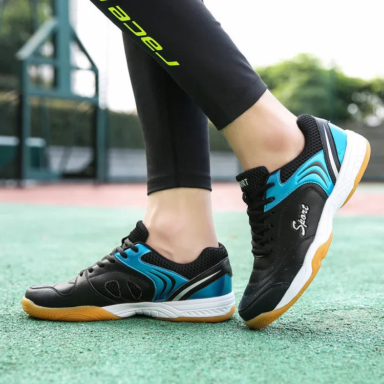 Black and blue athletic sneakers with mesh panels and gum soles, worn outdoors on a court