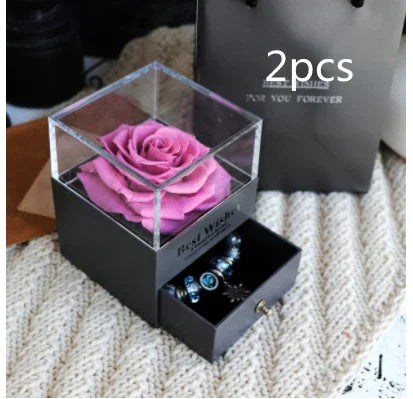 Black gift box with clear lid displaying pink preserved rose, drawer holding beaded bracelet