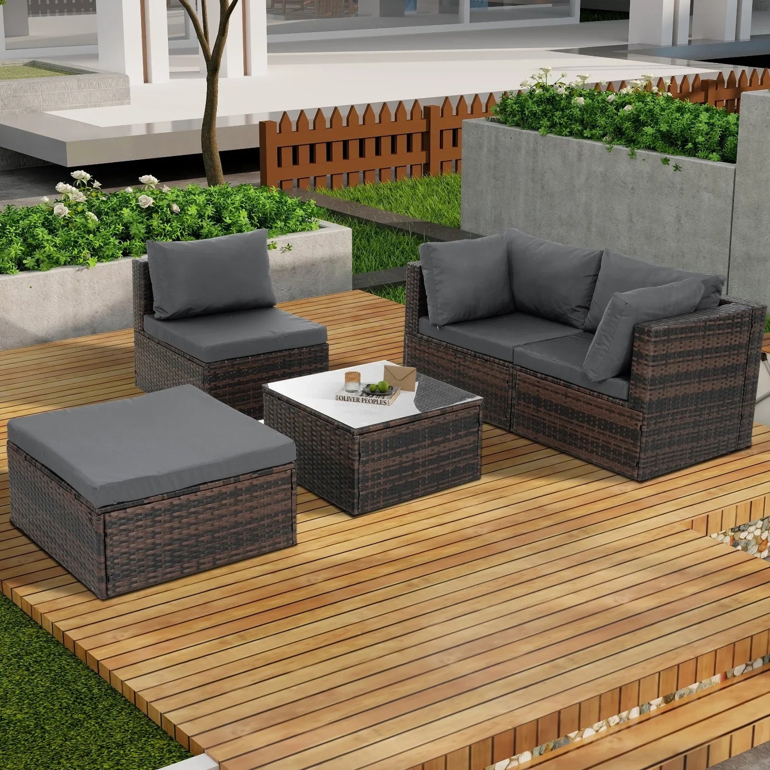 Modern outdoor seating set with dark rattan frame, gray cushions, and glass-top table on wooden deck