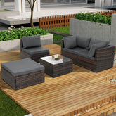 Modern outdoor seating set with dark rattan frame, gray cushions, and glass-top table on wooden deck