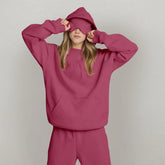 Woman wearing oversized pink hoodie and matching sweatpants, casual streetwear style.