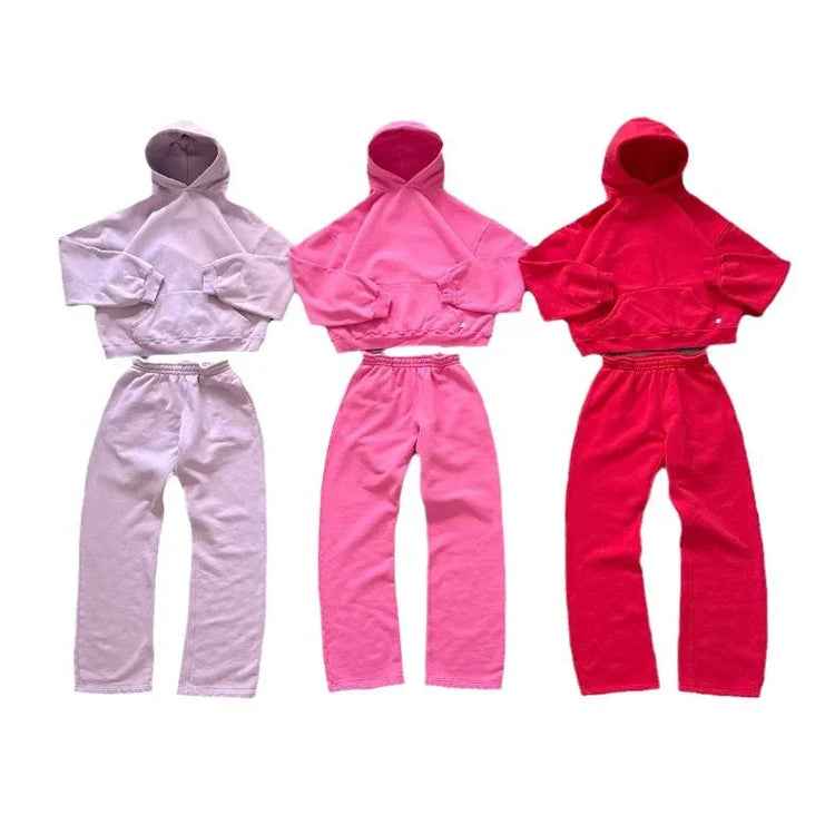 Three cropped hooded sweatshirts with matching jogger pants in pastel, pink, and red fleece, relaxed fit.