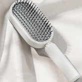 Modern white paddle hair brush with black bristles on a soft, textured fabric background