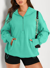 Woman wearing loose teal half-zip hoodie with kangaroo pocket and black shorts, casual streetwear style