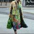 Colorful oversized long coat with nature-inspired print, loose fit, worn with green handbag.