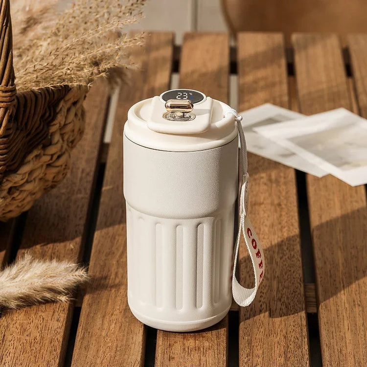 Matte white insulated travel mug with digital temperature display and strap on wooden table