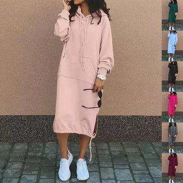 Woman wearing a loose pink hoodie dress with drawstring, front pocket, and white sneakers.