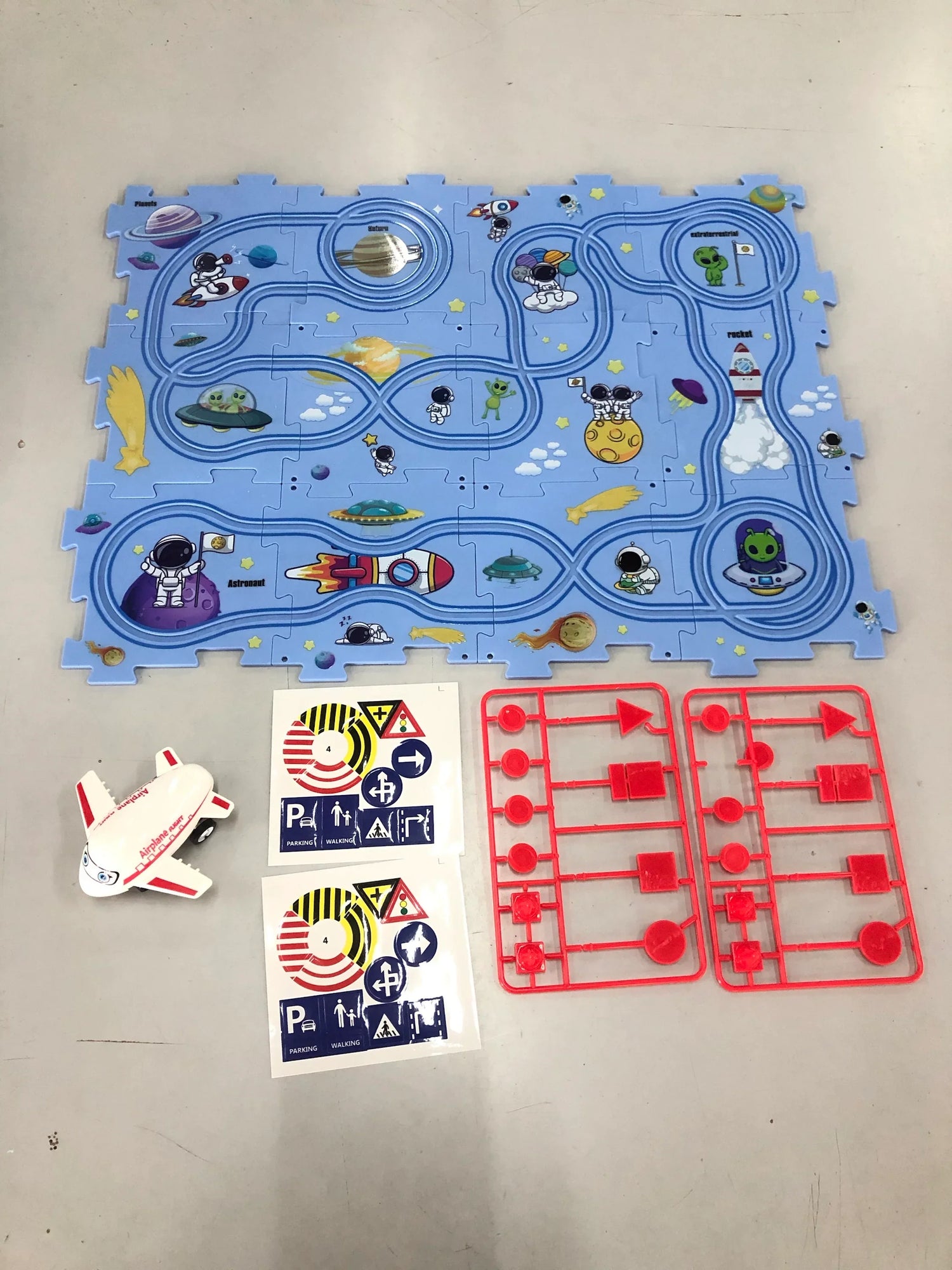 Children’s space-themed play mat with astronaut graphics, toy spaceship, stickers, and red plastic sign pieces.
