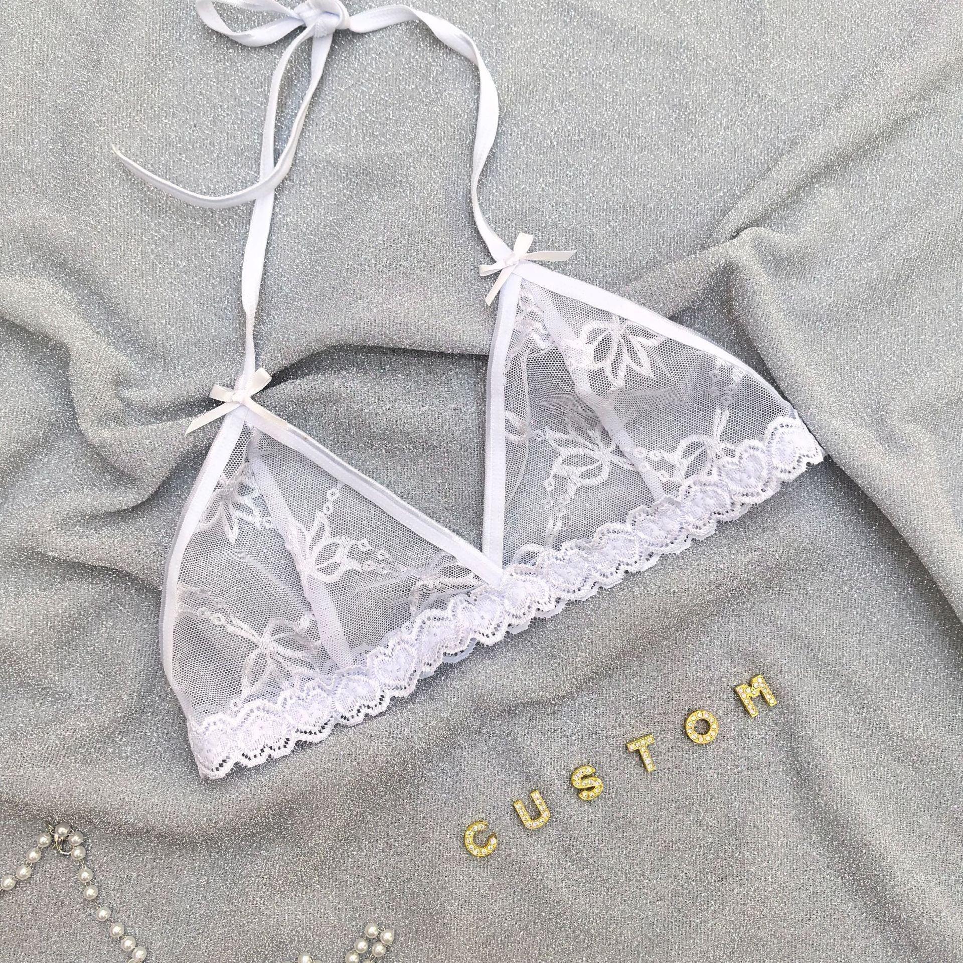 White lace bralette with floral embroidery and adjustable tie straps on a silver fabric background