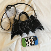 Black faux leather handbag with white spider web stitching, batwing shape, on beige fabric