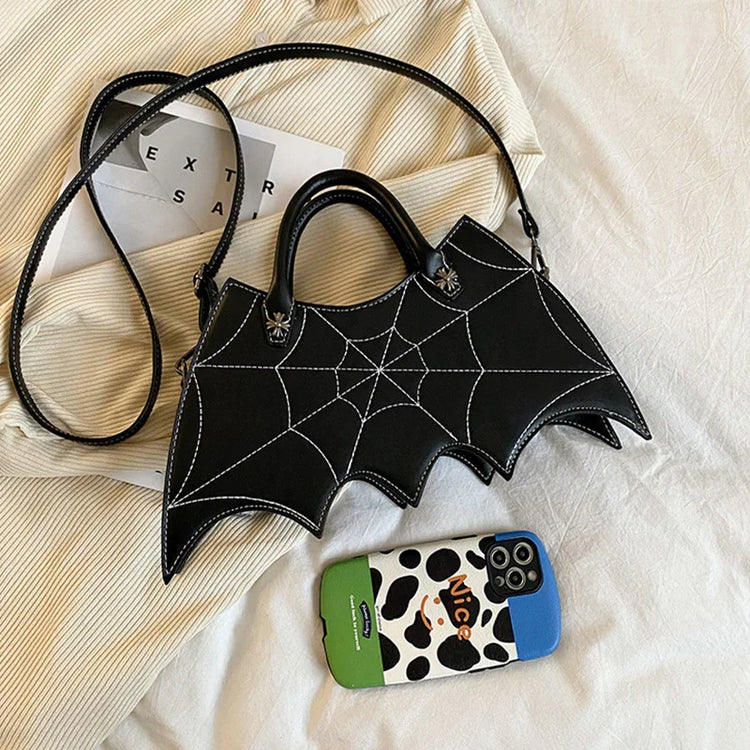 Black faux leather handbag with white spider web stitching, batwing shape, on beige fabric
