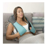 Woman relaxing on sofa wearing a teal and black ergonomic shoulder massager over casual loungewear.