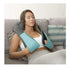 Woman relaxing on sofa wearing a teal and black ergonomic shoulder massager over casual loungewear.