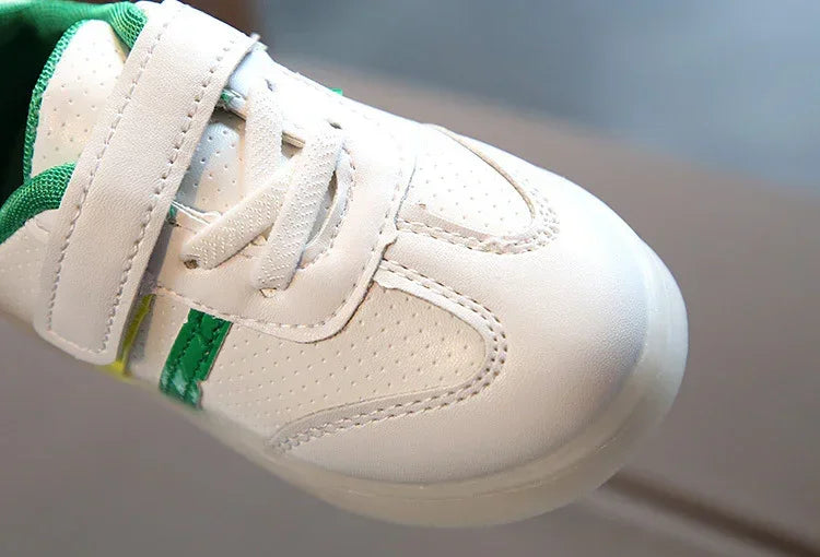 White perforated sneaker with green accents, velcro strap, and laces, close-up view